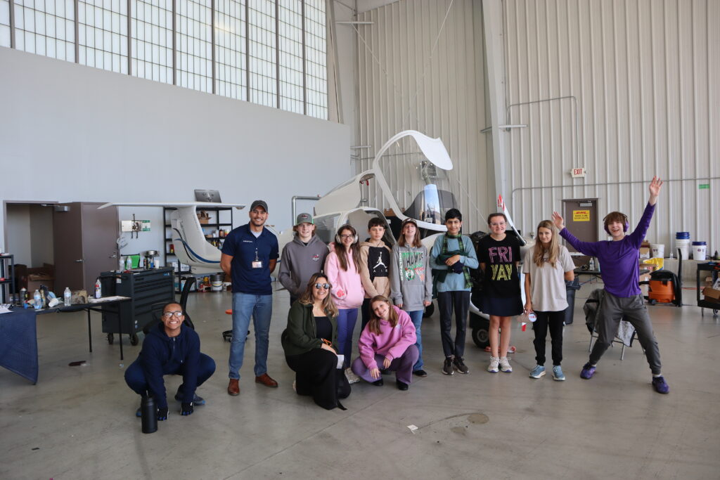 Students pose in front of a small plane at RVA Flyers during a field trip.