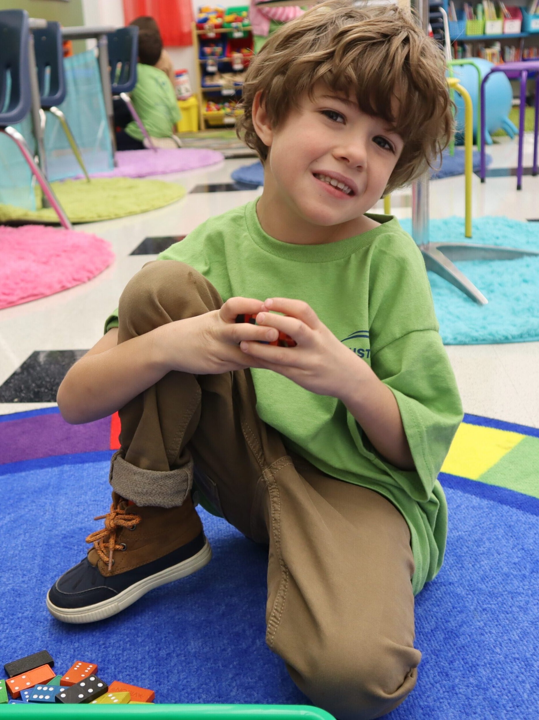 Student sitting on carpet holding dominos