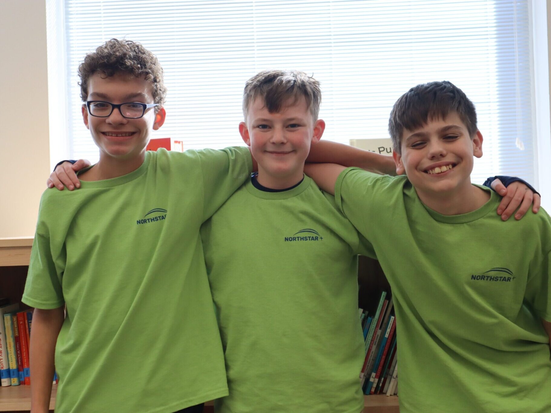 Three boys with arms around each other smiling at camera