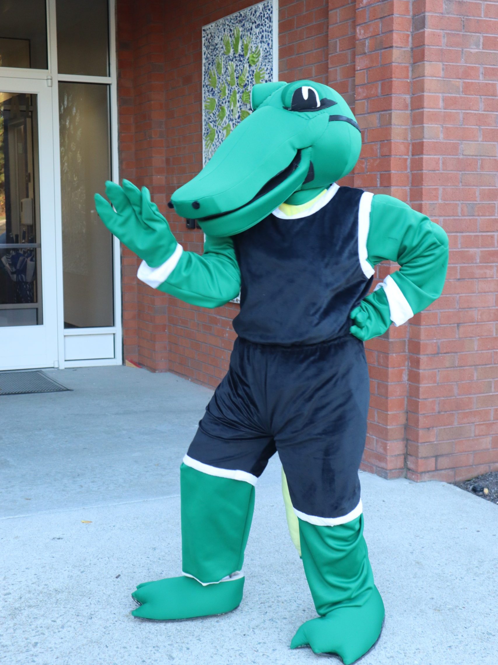 Navi (alligator mascot) waving in front of school building