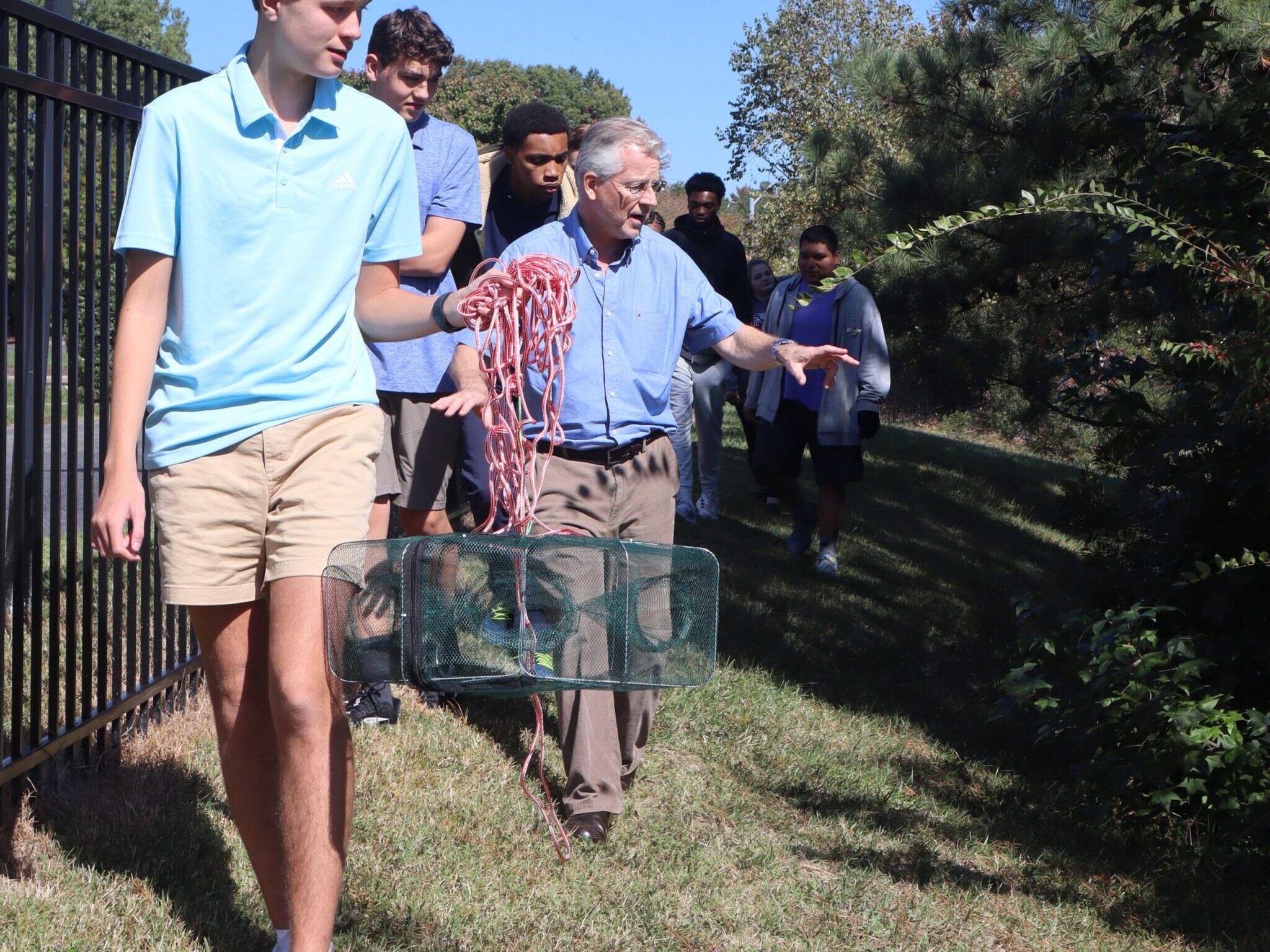 High school science students walking outside getting ready to set a fishing trap in pond.