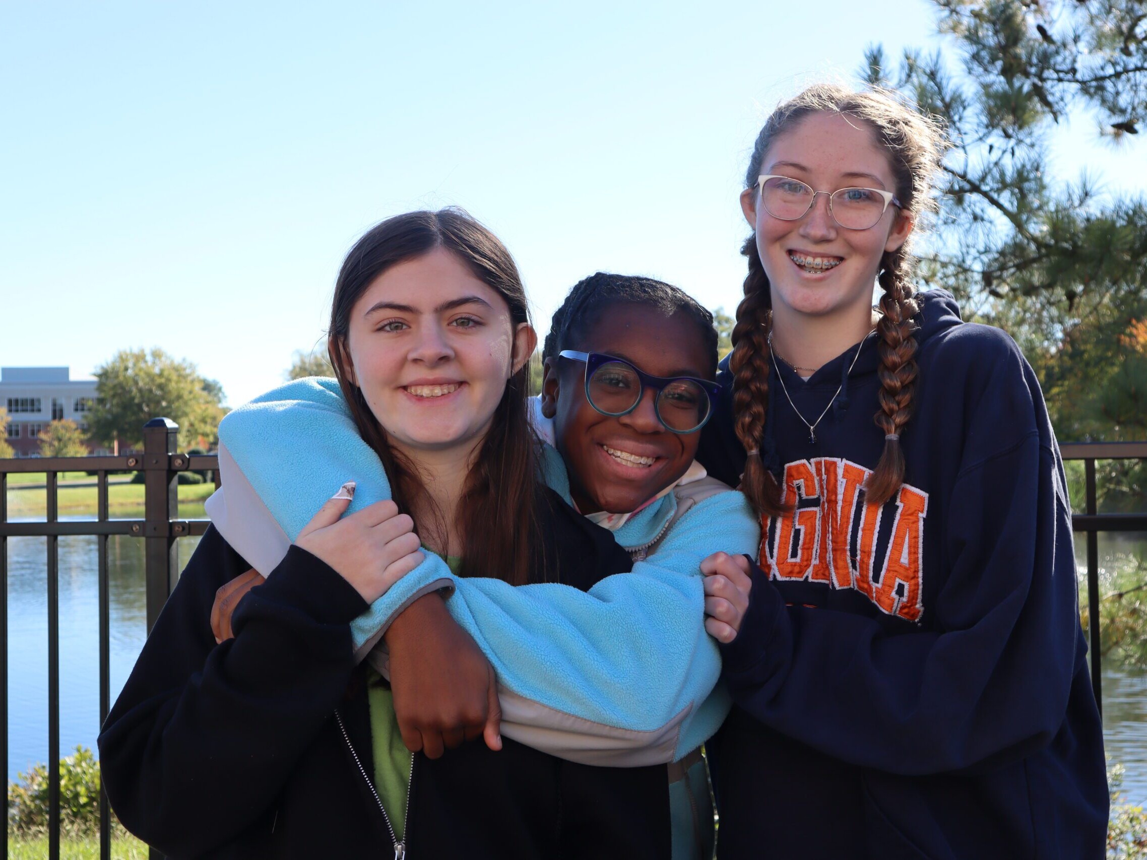 Three students smiling at camera in from of pond