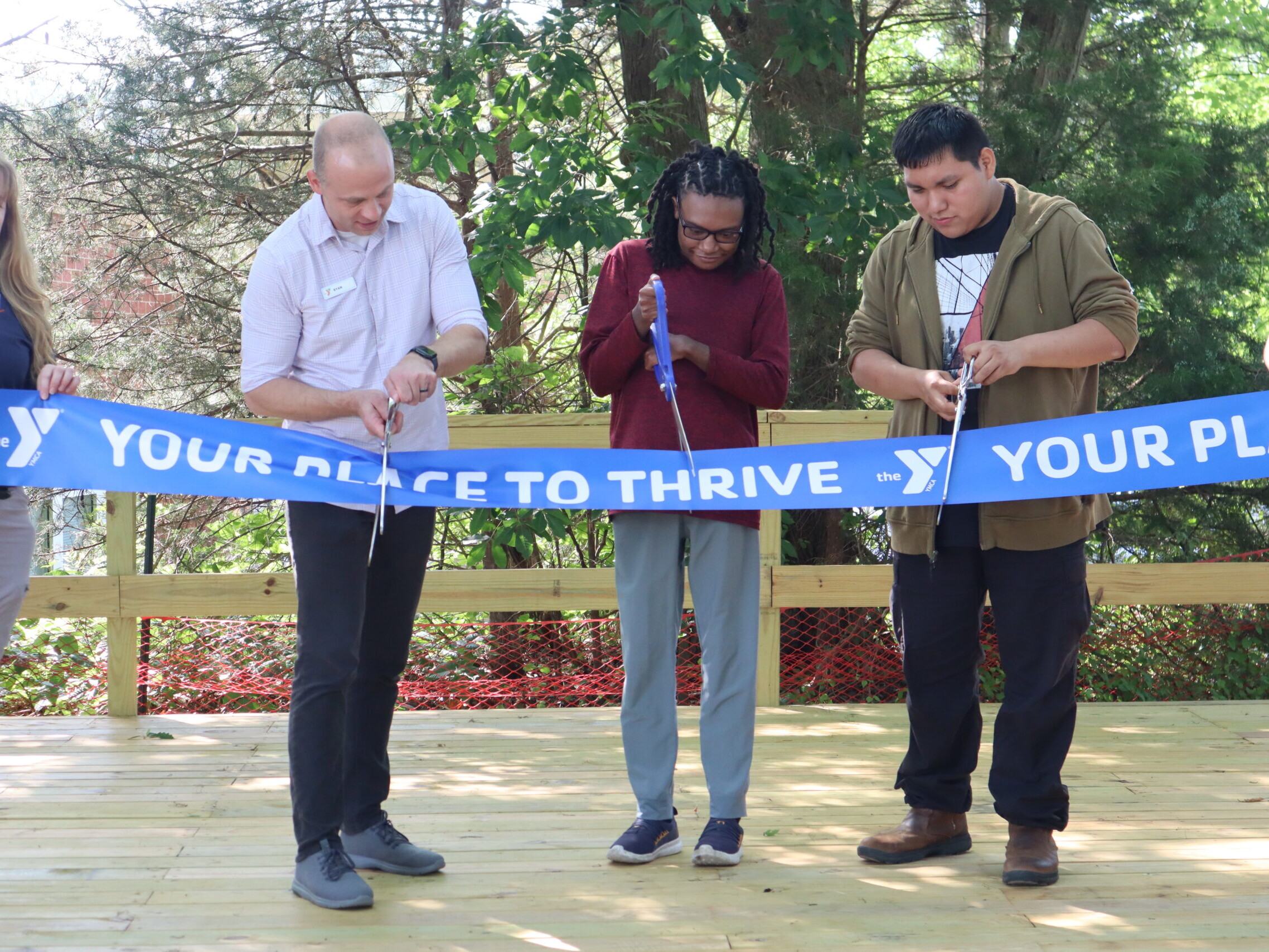 Students and YMCA empoyees stand side by side on the stage and cut a ceremonial blue ribbon.