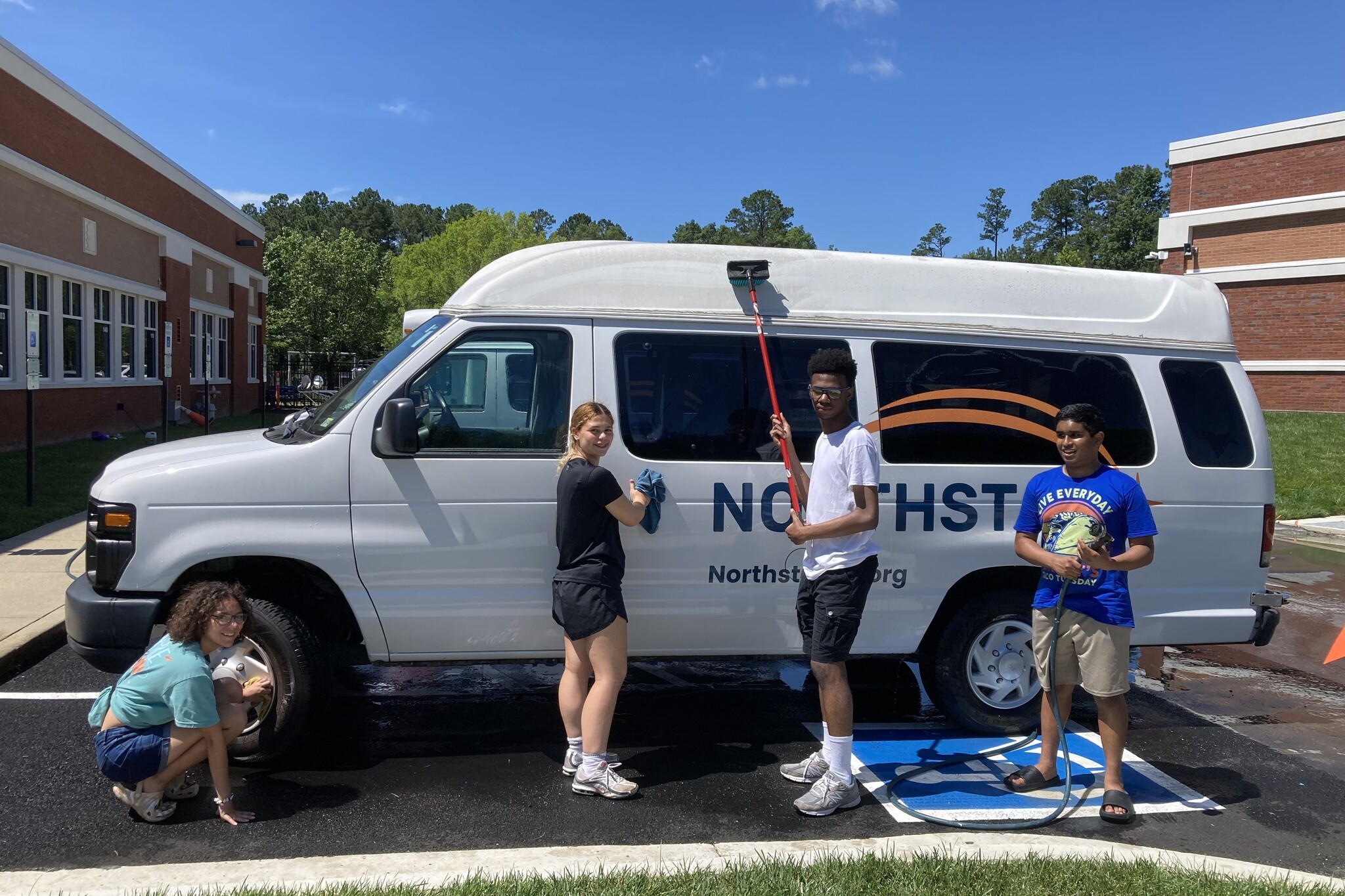Four teenagers from Richmond's Catholic Heart Work Camp pose holding cleaning equipment in front of a Northstar bus.