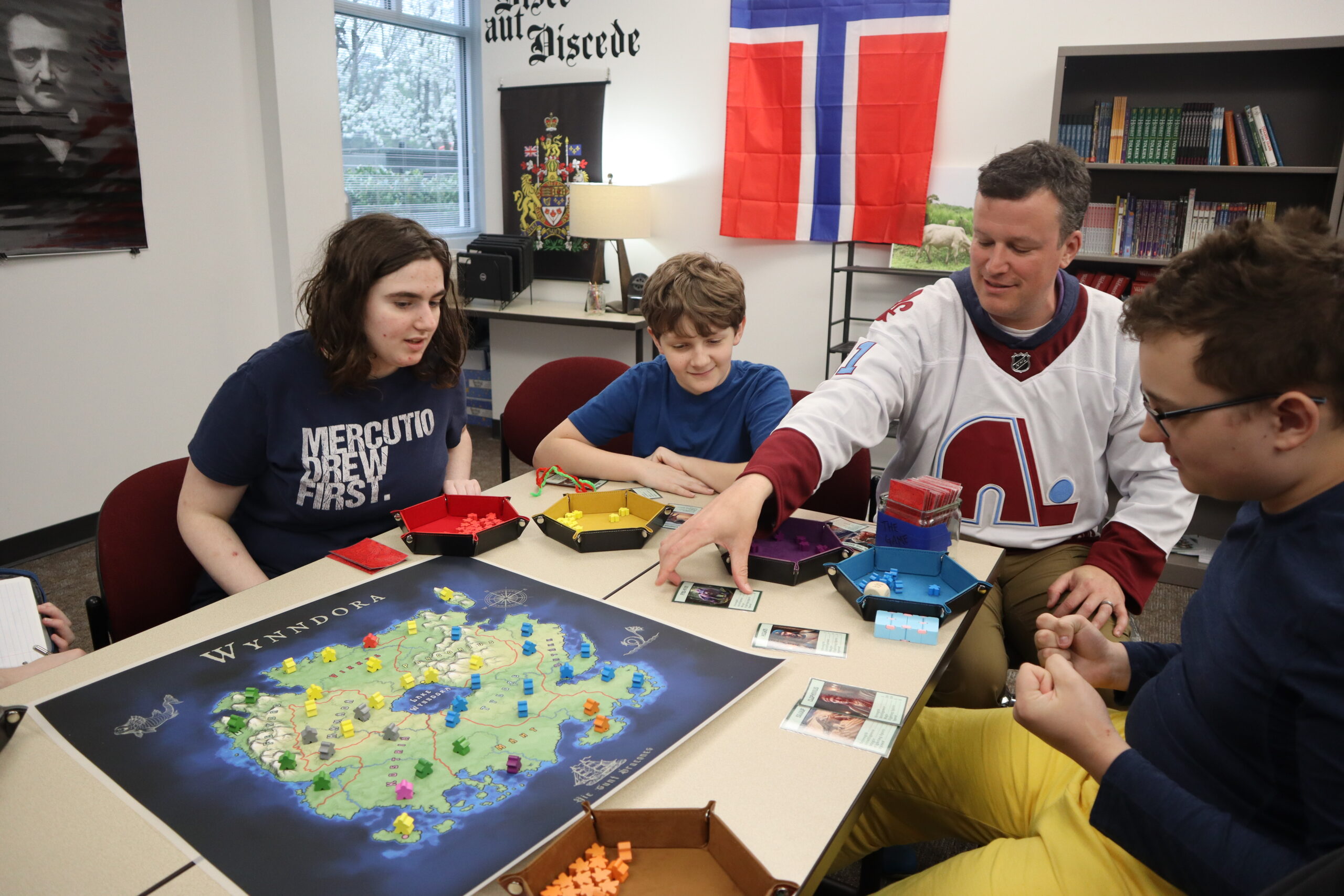 A teacher and students sit at a table together playing an educational board game.