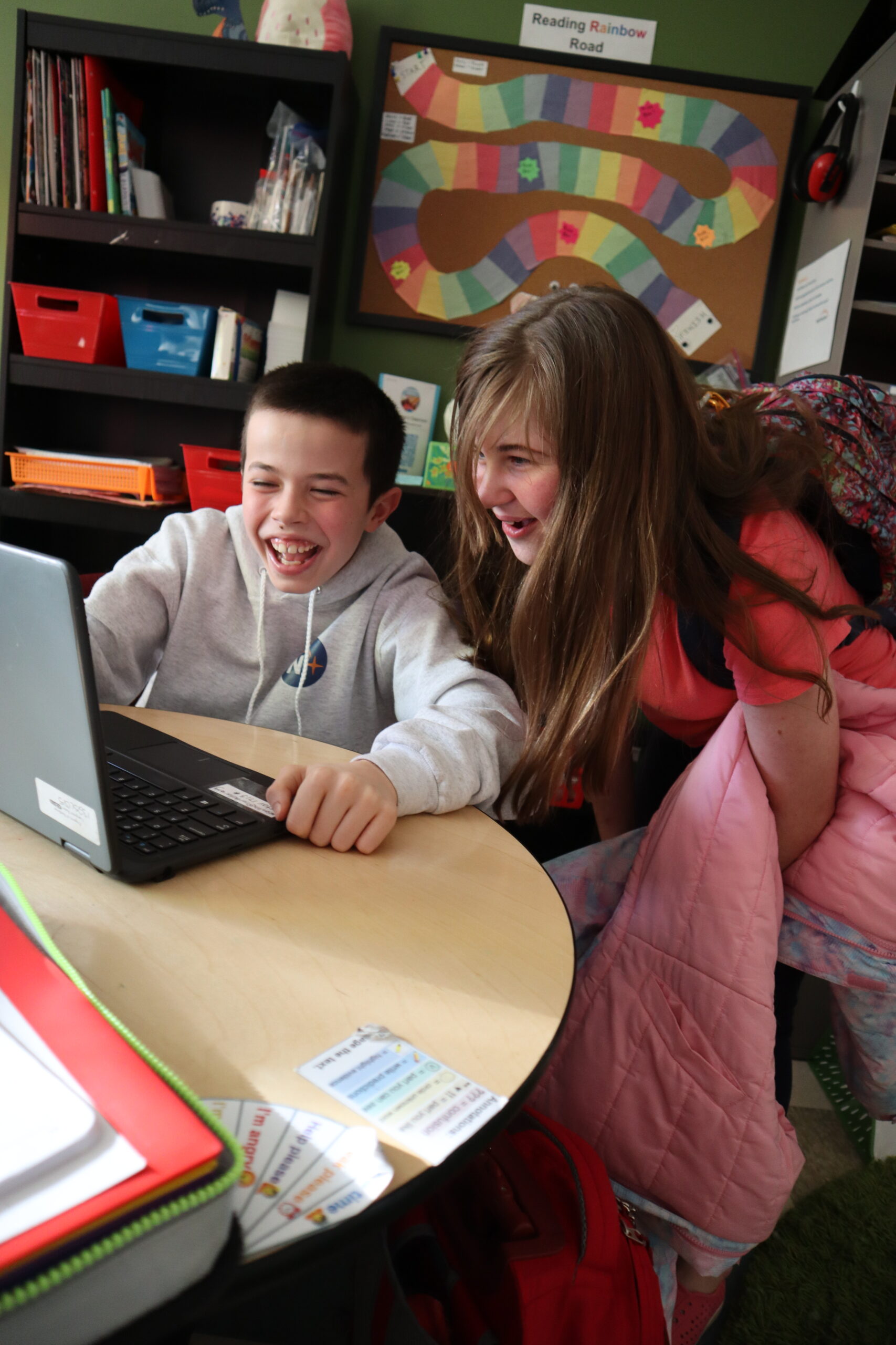 Middle schoolers laugh and look at a laptop together.