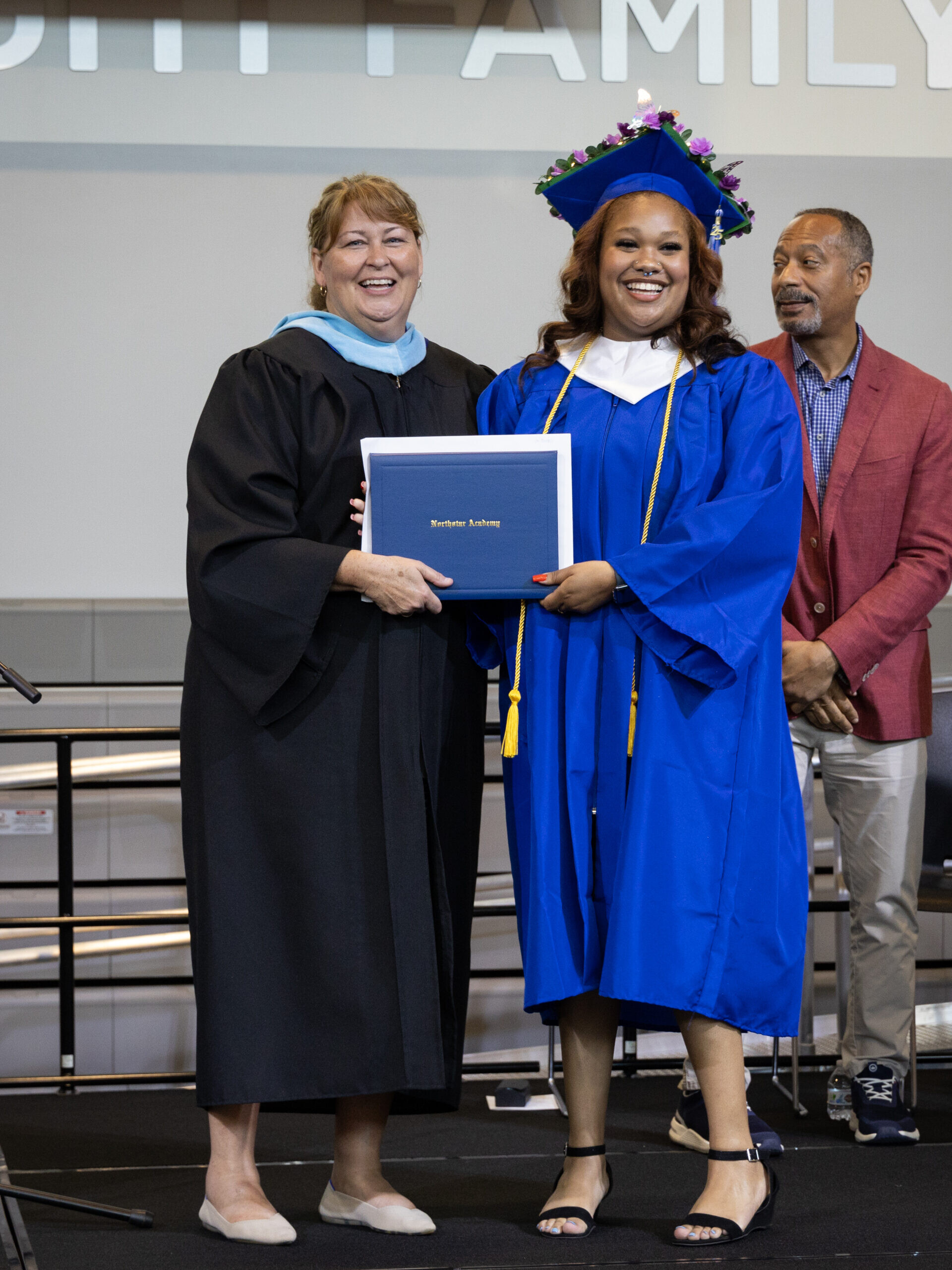 A graduate smiles as they receive their diploma from the Head of School.