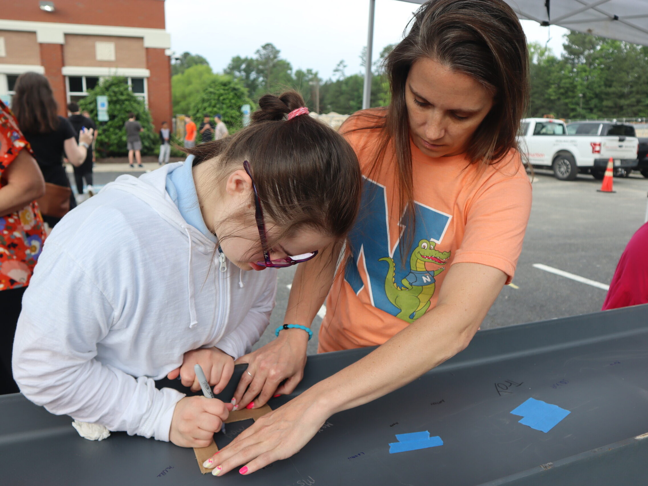 A staff member helps a student sign their name on a large metal I beam.