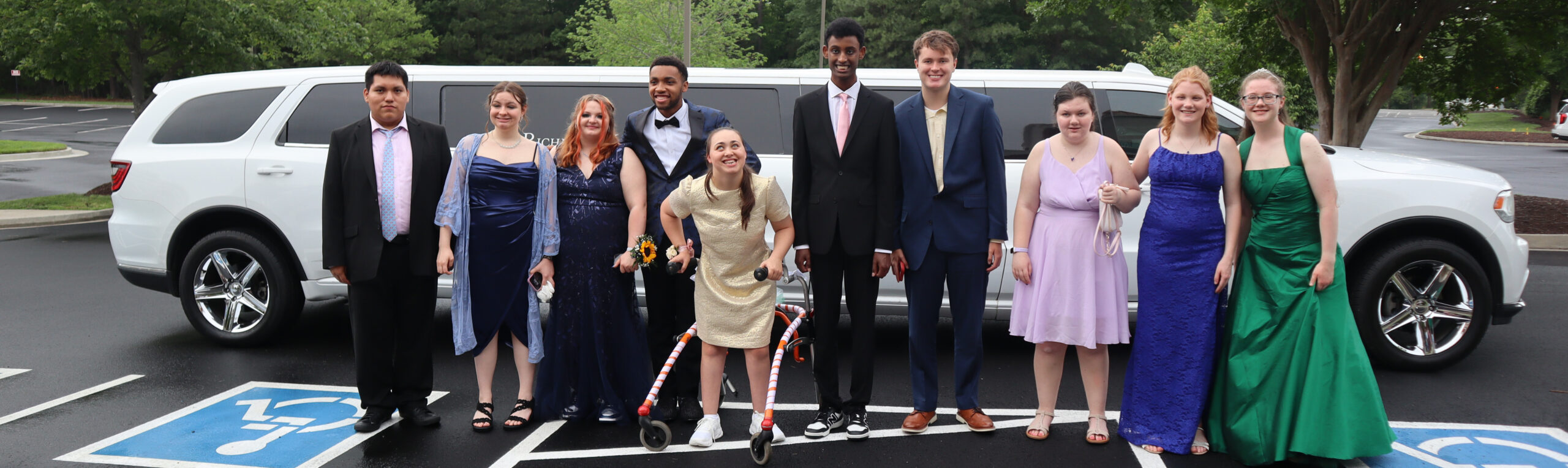 Students pose in front of a limo all dressed up for Prom.