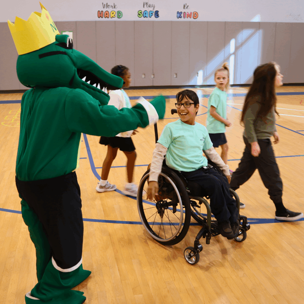 Navi the Gator and student Navi the Gator waves to passing students at an assembly.