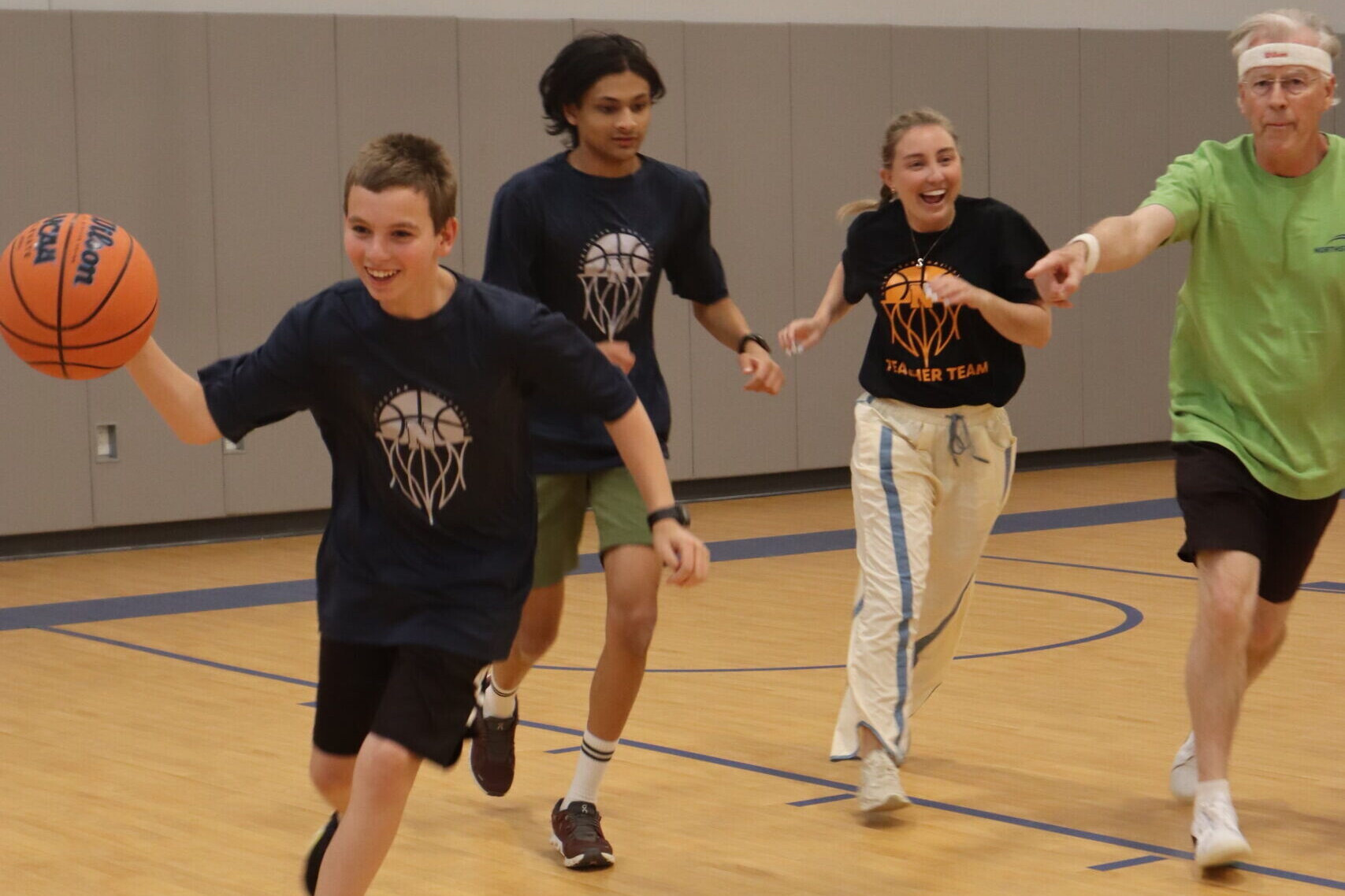 A student dribbles the ball, a teammate and two teachers close behind him.