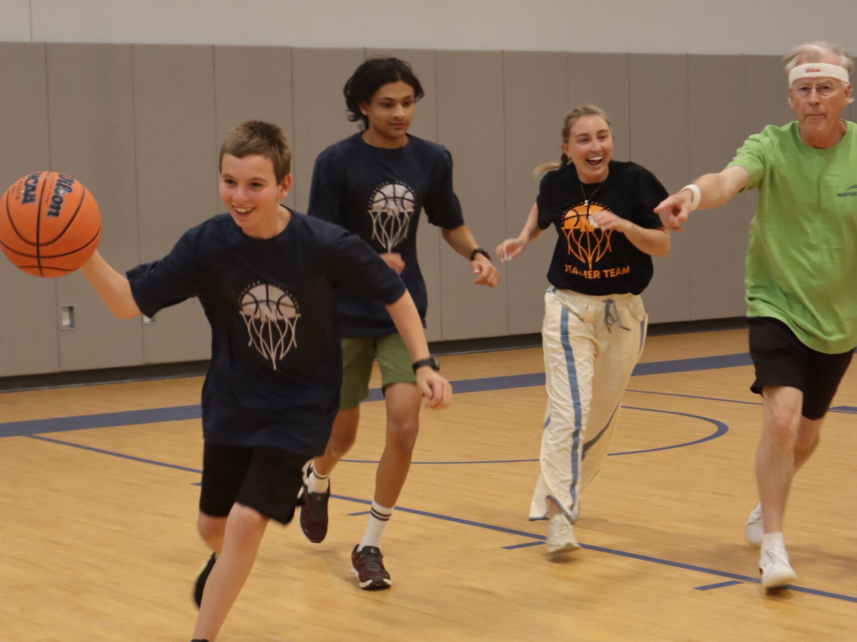 A student dribbles the ball, a teammate and two teachers close behind him.