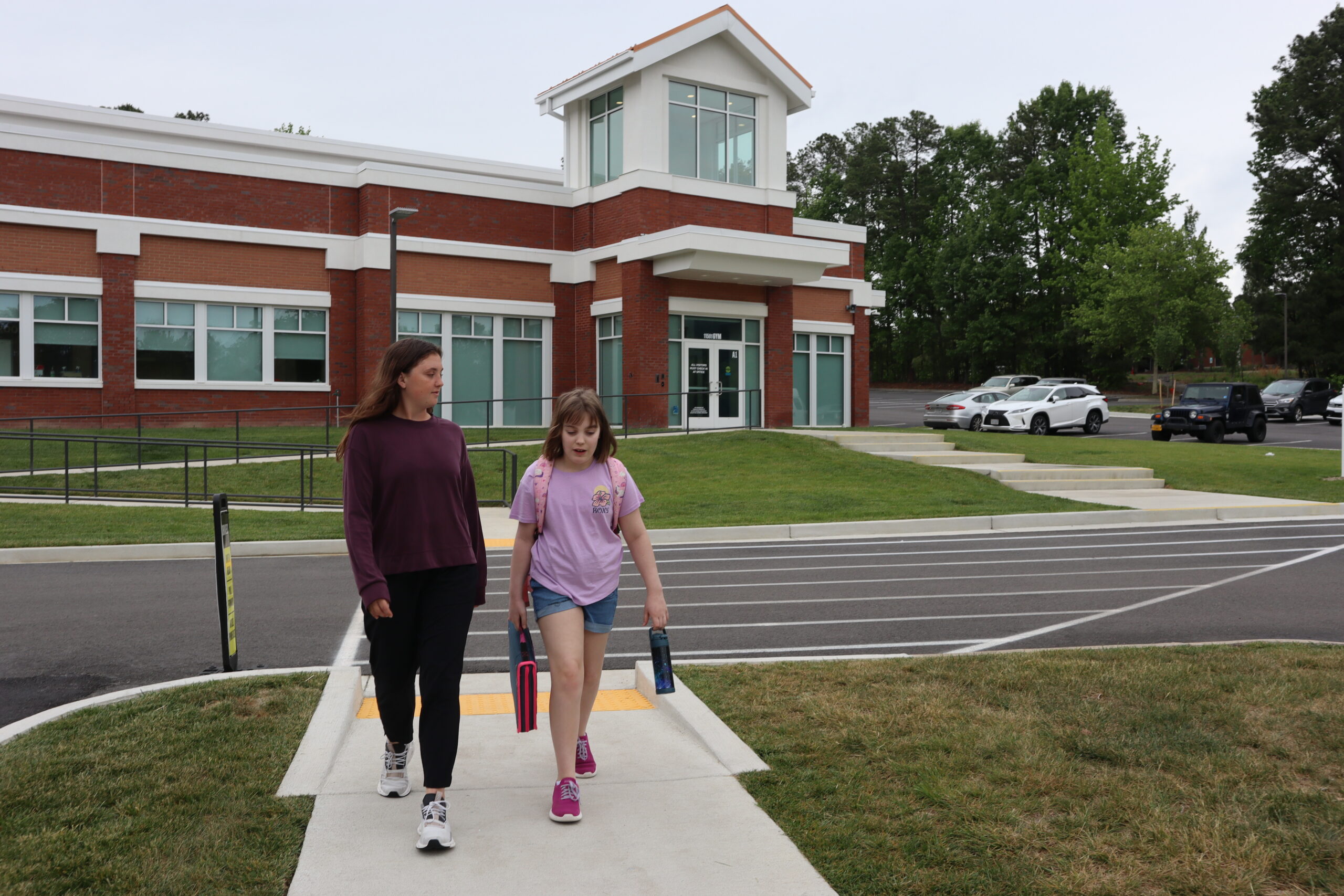 A student teacher walks alongside a middle schooler back to the main building from the gymnasium.