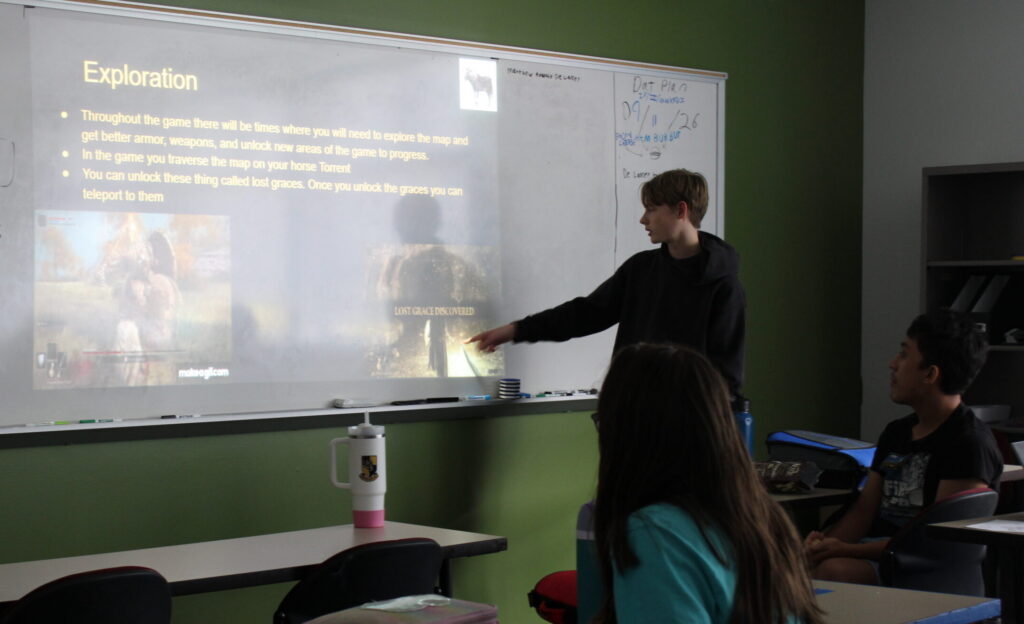 Flavor Presentations A student stands at the front of a classroom and gestures to a projected image video game mechanics.